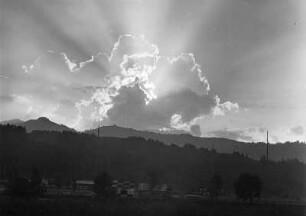Wolkenbilder. Wolken mit untergehender Sonne über hügeliger Landschaft