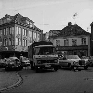 Hude: Einmündung Mühlenstraße vorn mit Absperrung: dahinter parkender Lkw und Pkws, links Mann: hinten links Bekleidungsgeschäft Gebr. Petersen: in der Mitte Einmündung Besttorstraße: hinten rechts Wohn- und Geschäftshäuser