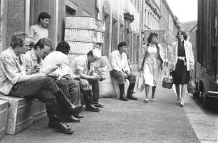 Pause der Fleischer : Waldheim. Eine Gruppe von Fleischern die vor dem Laden auf der Straße ihre Pause machen. Zwei Frauen gehen an ihnen vorbei