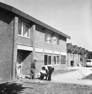 Freiwillige Feuerwehr: Stormarnstraße: Feuerwehrgerätehaus vor Fertigstellung: links zwei Arbeiter mit Schubkarre beim Verlegen von Gehwegplatten im Eingangsbereich: hinten rechts Gerüst: davor Pkw und Lieferwagen