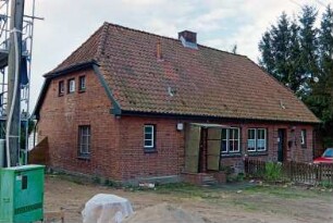 Blumendorf 3: traufständige Doppelkate aus Backstein: Straßenfront: Eingangstüren, Hausnummer, Sprossenfenster: vorne Vorplatz, Zaun, Auto: im Vordergrund links Strommast, Stromkasten, Gerüst [angeschnitten]: 29. April 2003