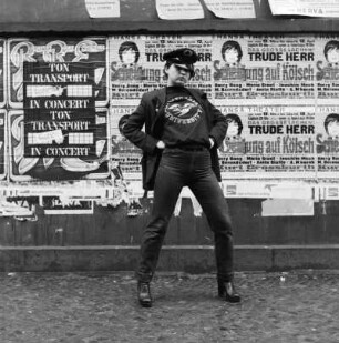 Frau mit Schirmmütze vor einer Wand mit Plakaten