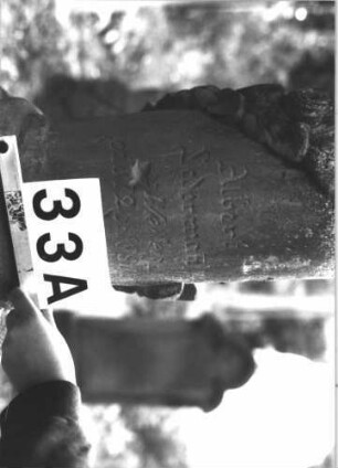 Grabstein 33 (Index: 99898747) Material: Sandstein Zustand: stark verwittert Maße HxBxT: 102x45x20 cm Beschreibung: aufgesockelte Stele mit Konvexbogenabschluss, oben mit Palmette und Voluten Symbolik: Palmette, Voluten: Grabstein 33A