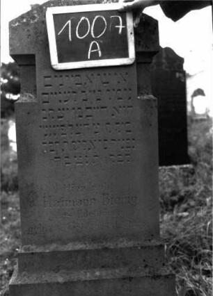 Grabstein 1007 (Index: 100103972) Material: Sandstein Zustand: gut erhalten Maße HxBxT: 131x44x16 cm Beschreibung: unten mehrfach getreppte Stele auf getrepptem Sockel, Dreiecksabschluss, seitlich durch Einzüge als nach oben weisener Pfeil gestaltet: Grabstein 1007A