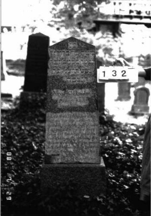Grabstein 132 (Index: 100101088) Material: Granit Zustand: leicht verwittert Maße HxBxT: 155x47x20 cm Beschreibung: Stele, Sockel, giebelartiger Abschluß: Grabstein 132