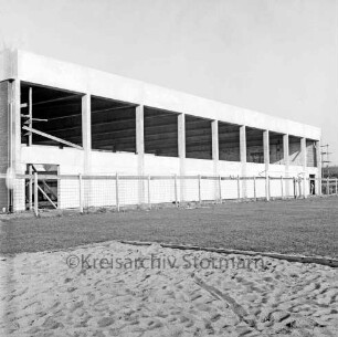 Sporthalle: Realschule [später Dietrich-Bonhoeffer-Realschule]: Am Schulzentrum: in Bau: Rohbau: Außenansicht: Längsseite Verblendung mit Waschbetonplatten: Bauzaun: im Vordergrund Rasen, Sandfläche