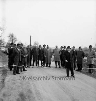 Vinzier: Gemeindestraße zwischen Vinzier und Neverstaven: Einweihung: Durchtrennung des Bandes durch Bürgermeister Fritz Krasmann im Beisein von Landrat Wennemar Haarmann, Amtsvorsteher Hans Hagen und Gästen