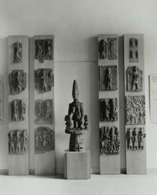 Ausstellungswand mit 16 Bronzereliefs und hölzernem Maskenaufsatz mit Göttin der Fruchtbarkeit (Ododua) und Begleitern