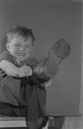 Ein Junge (Lothar) zieht sich einen Stiefel an