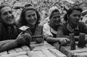 Vier Trümmerfrauen, posierend hinter einem Ziegelstapel