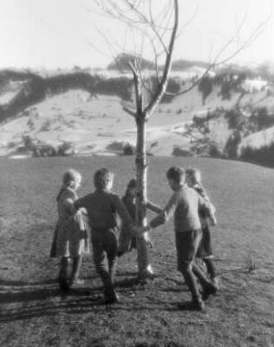Kinderbilder. Kinder beim Ringelreihen um einen Baum