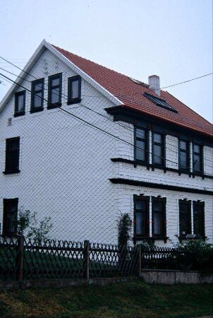 Haus mit heller Schindelverkleidung, renoviert; Jägerzaun