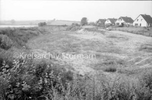 Kieskuhle am Moorteich: rechts Häuser: davor Straße mit parkendem Pkw, Tor und Zäunen: im Vordergrund Fläche mit Heide: im Hintergrund der Moorteich und Knicklandschaft: 23. August 1985