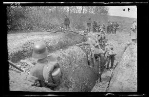 Übungsgelände I bei Mouzon (Dep. Ardennes, Frankreich): Soldaten mit Stahlhelm und voller Ausrüstung am Ende eines Grabens beim Hinausblicken, im Hintergrund oberhalb des Grabens weitere Soldaten und Offiziere beim Abrücken ("im Graben")