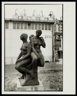 Eine Skulptur mit drei Frauen vor Industriearchitektur