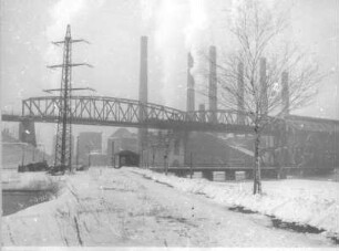 Hirschfelde. Braunkohlenkraftwerk. Teilansicht mit Kühltürmen, Schornsteinen und Stahlfachwerkbrücke der Grubenbahn, im Vordergrund Mast einer Hochspannungsfreileitung