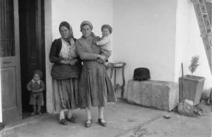 Die erste Kolonistenfamilie : Zwei Frauen mit Kleinkindern vor einem Haus