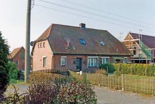 Blumendorf (2): traufständige Doppelkate aus Backstein: Straßenfront: Eingangstüren, Hausnummer, Fenster: Giebelseite: hinten links Stallgebäude: vorne Vorplatz, Strommast: Vorgarten, Zäune, Hecken: rechts Nachbarhaus mit Gerüst: 22. April 2003