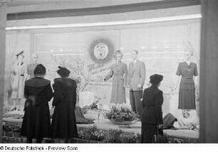 Besucherinnen vor einem Schaufenster mit Damen- und Herren-Bekleidung
