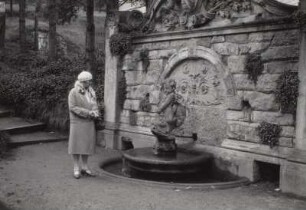Putto auf einem Dephin reitend : Hulda Hanisch, vor einem Wandbrunnen in einem Park stehend