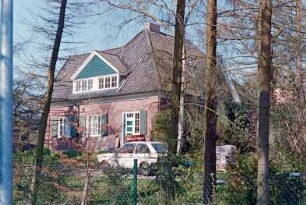 Struhbarg 44: traufständiges Wohnhaus aus Backstein: Giebelseite mit seitlichem Querbau, Seitentür, breite Giebelgaube mit Verbretterung: rechts Straßenfront [halb verdeckt]: im Vordergrund Maschendrahtzaun zu Beethovenstraße