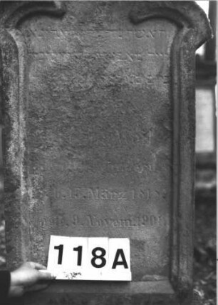 Grabstein 118 (Index: 99898916) Material: Sandstein Zustand: stark verwittert Maße HxBxT: 137x57x20 cm Beschreibung: aufgesockelte Stele mit seitlich spitz auskragendem Dreipassbogenabschluss, unterer Sockel felsartig gearbeitet Besonderheit: ergänzt nach Gräberverzeichnis: Grabstein 118A