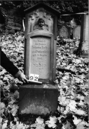 Grabstein 92 (Index: 100091032) Material: Sandstein Zustand: verwittert Maße HxBxT: 0x0x0 cm Beschreibung: Stele auf Sockel mit Dreiecksgiebel Symbolik: Engelskopf über Inschrift: Grabstein 92