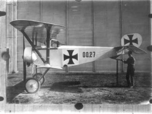 Einsitziges Doppeldecker-Flugzeug 00.27 mit Propellerantrieb (um 1910/1914), eingesetzt von den deutschen Luftstreitkräften im I. Weltkrieg. Seitenansicht mit Pilot. Fotografie (Nr. 18); an eine Wand gepinnt