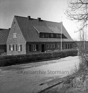 Amt Lütjensee: Amtsverwaltung: Amtshaus: davor Hecke und Fahnenmasten: vorn Sandweg: hinten links weiteres Gebäude