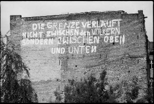 Brandmauer mit Inschrift "Die Grenze verläuft nicht zwischen den Völkern / sondern zwischen oben und unten"