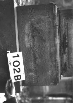 Grabstein 102 (Index: 99898883) Material: Sandstein Zustand: etwas angewittert Maße HxBxT: 144x50x29 cm Beschreibung: aufgesockelte Stele, oben abgeflachter Giebelaufsatz, darauf doppelter Rundbogen mit Blattornamenten, unterhalb des Aufsatzes Zinnenfries Symbolik: Zinnenfries, Blattornamente: Grabstein 102B