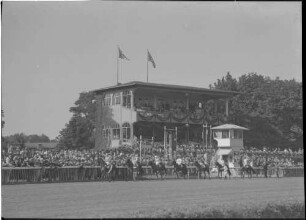 Hoppegarten: Ehrentribüne [mit Hakenkreuzfahnen], Vordergrund Reihe Reiter