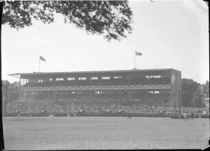 Hoppegarten: große Tribüne [mit Hakenkreuzfahnen], Vordergrund Bäume