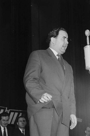 Portrait Heinz Quermanns während eines Auftritts bei der Ziehung der 52. Spielwoche des VEB Zahlenlotto, im Hintergrund Mitglieder des Rundfunk-Blasorchesters Leipzig