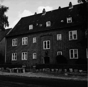 Hebbelstraße: Ausbau: vorn unbefestigte Straße, Stapel mit Gehwegplatten und Mülleimer: dahinter Wohnhäuser der Gemeinnützigen Baugenossenschaft Bad Oldesloe mit Vorgärten