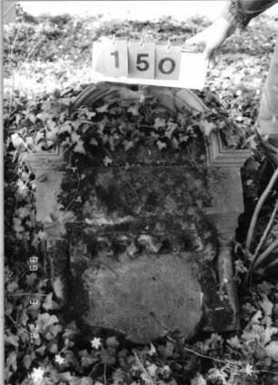 Grabstein 150 (Index: 99792260) Material: Sandstein, weiße Marmorplatte Zustand: verwittert, untere Stelenhälfte fehlt, Abschluß beschädigt, Stele liegend Maße HxBxT: 84x66x32 cm Beschreibung: ädikualartige Stele mit Halbsäulen, eingezogener Rundbogenabschluß mit Verdachung, rechteckige Schriftplatte Symbolik: gestelztes Rundbogenfries: Grabstein 150