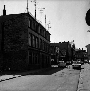 Hagenstraße: hinten links Wohnhäuser vor Abriss: dazwischen Hinweisschild zur Volksbank Bad Oldesloe: hinten rechts Giebel des Stadthauses und Hauptgebäude der Kreissparkasse Stormarn: rechts Pkws: 8. August 1975