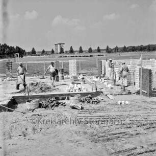 Sporteinrichtungen: Mühlenredder: Sportlerheim: Neubau: rechts zwei Maurer beim Hochziehen der Grundmauern: links zwei Maurer mit Zementsack und Eimer auf Fundament: davor zwei Mischbottiche und Ziegel: dahinter Sportplatz: hinten hinter Baumreihe achtgeschossiges Punkthaus im Stadtteil Klosterbergen am Eichenbusch