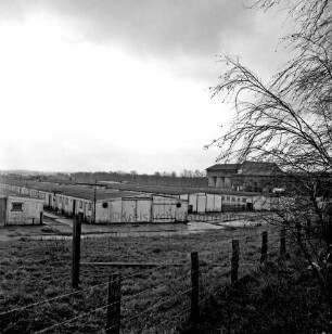 Heinrichshof, Gut: stillgelegte Schweinemastanlage: verfallene Schweineställe: im Hintergrund rechts Futtermittelgebäude: vorn Böschung mit Stacheldrahtzaun und Büsche