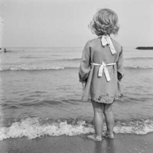Kleines Mädchen steht im Wasser der ankommenden Wellen am Strand von Henkenhagen (heute: Ustronie Morskie)