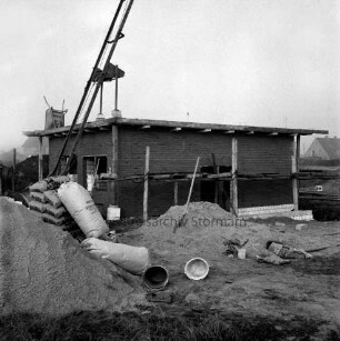 Wasserversorgung: Wasserwerk für Neubaugebiet Kellerberg-Süd: Rohbau: vorn Sandhaufen, Zementsäcke und Eimer: hinten links Schubkarre auf Dach und Materiallift: hinten Einfamilienhäuser