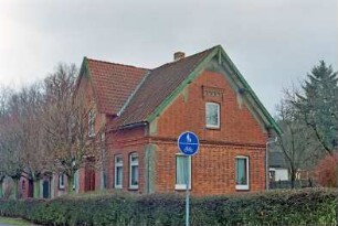 Sattenfelde: Bahnhofstraße 38: traufständiges Backsteinhaus: Straßenfront, Mittelrisalit mit Dreiecksgiebel, Eingangstür: Giebelseite: davor links Baumreihe, Hecke