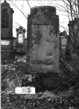 Grabstein 28 (Index: 100114947) Zustand: leicht verwittert, Textplatte fehlt Maße HxBxT: 164x59x21 cm Beschreibung: Stele auf Sockel, im oberen Teil beidseitig schulterartig abgerundet, flacher Giebel mit Stern, eingesetzte Textplatte: Grabstein 28