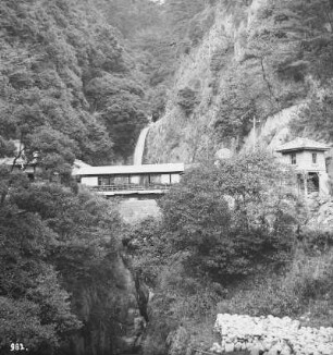 Honshū. Nunobiki-Wasserfall bei Kobe mit überdachter Brücke und Gebäuden beiderseits der Schlucht