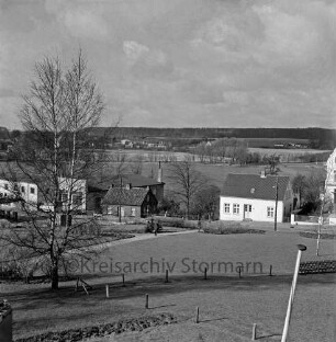 Grünanlage zwischen Markt, Matthias-Claudius-Schule und Ahrensböker Straße: Rasen, Zäune, Fußwege, Birke: rechts im Vordergrund Spitze von Fahnenstange: Bildmitte Häuser an Ahrensböker Straße, dahinter Herrenteich
