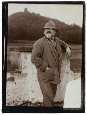 Portrait Max Slevogt an einer Turmzinne lehnend auf dem Turm seines Anwesens Schlossgut Neukastel : Max Slevogt an einer Turmzinne lehnend, vermutlich auf dem Turm seines Anwesens Schlossgut Neukastel, im Hintergrund wohl die Burgruine Neukastel.