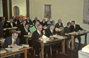 Kreistagssitzung: Kreisberufsschule [Bad Oldesloe]: Grabauer Straße / Ecke Lorentzenstraße: Aula: Kreistagsmitglieder an Schulbänken, darunter Gertrud Lege