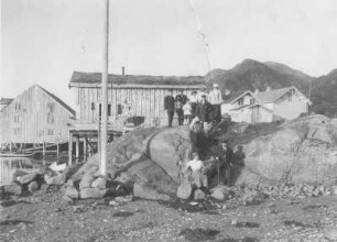 Digermulen auf Hinnöy (Lofoten)/ Norwegen: Gruppenbildnis mit Touristen gegen Fischerhäuser in einer Bucht des Vest-Fjords und Digermulenkollen : Nordlandreisen. Norwegen. Digermulen auf Hinnöy (Lofoten). Gruppenbildnis mit Touristen gegen Fischerhäuser in einer Bucht des Vest-Fjords und Digermulenkollen