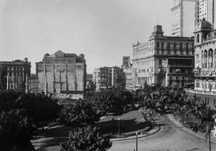 Innenstadt von São Paulo? : Hochhäuser auf der rechten Seite. Im Vordergrund eine Straße, die die von einer Baumallee gesäumt wird. Links eine Ruine eines Gebäudes.