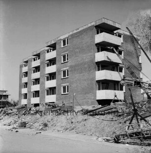 Ehmkenberg: Neubau: Wohnblock vor Fertigstellung: vorn Stapel mit Gerüsten, Erdhaufen, Bauschutt, Stromleitung, Ziegelstapel, Bagger und Förderbänder: hinten links Wohnblock